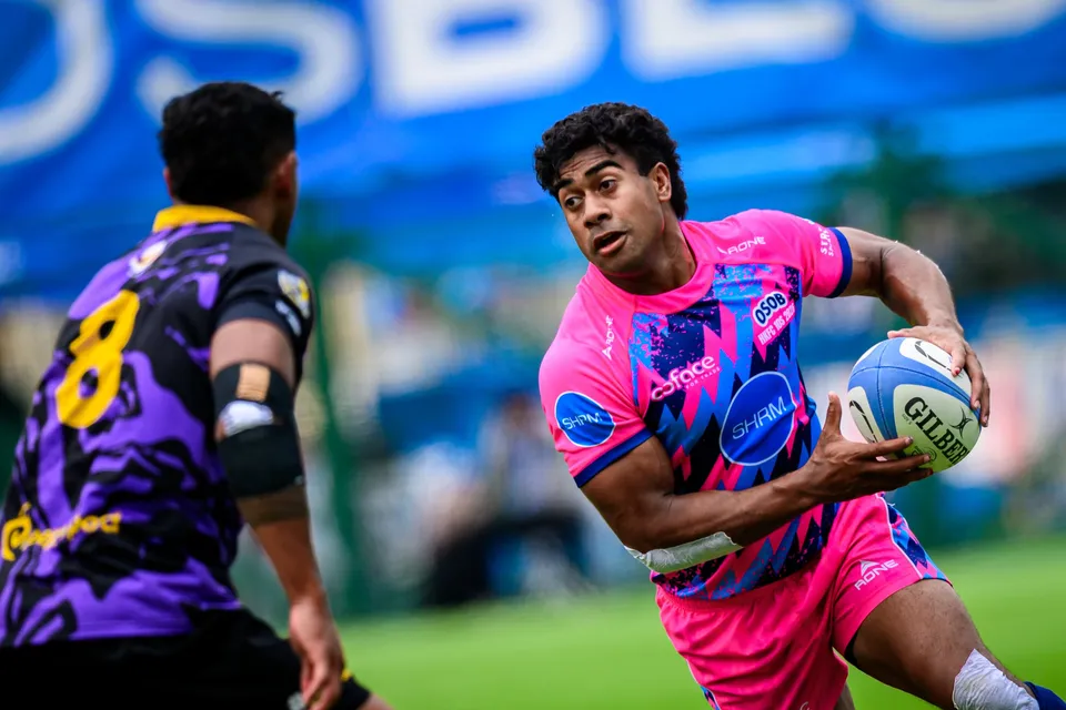 Close view of an OSOB player in pink holding the ball, looking to pass, with a purple number 8 opponent in front