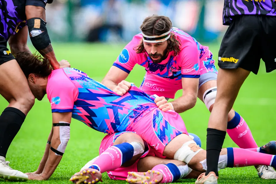 OSOB player lies bound over a pile of bodies at a ruck while a bearded team-mate in a headband leans in above