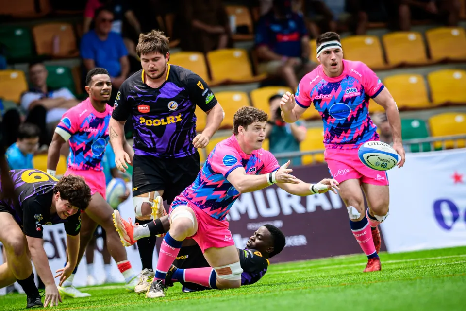 OSOB player flicks the ball away from the ground as a team-mate runs on and a purple-kit opponent looks on