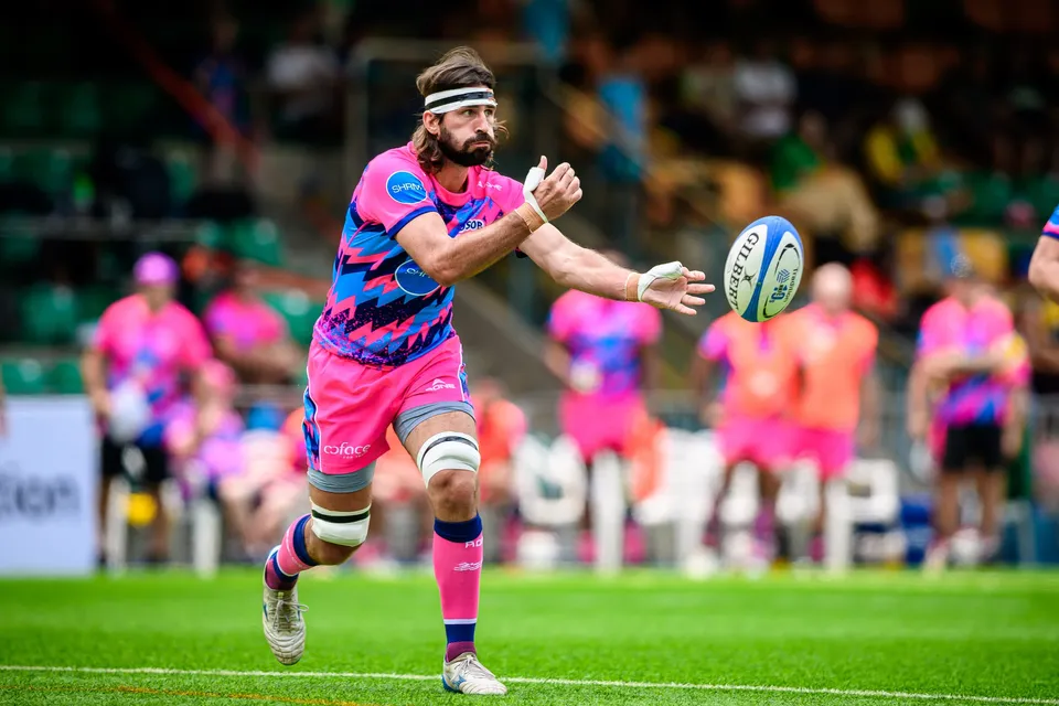 Bearded OSOB player in a headband passes the ball one-handed while pink-shirted team-mates wait behind on the touchline
