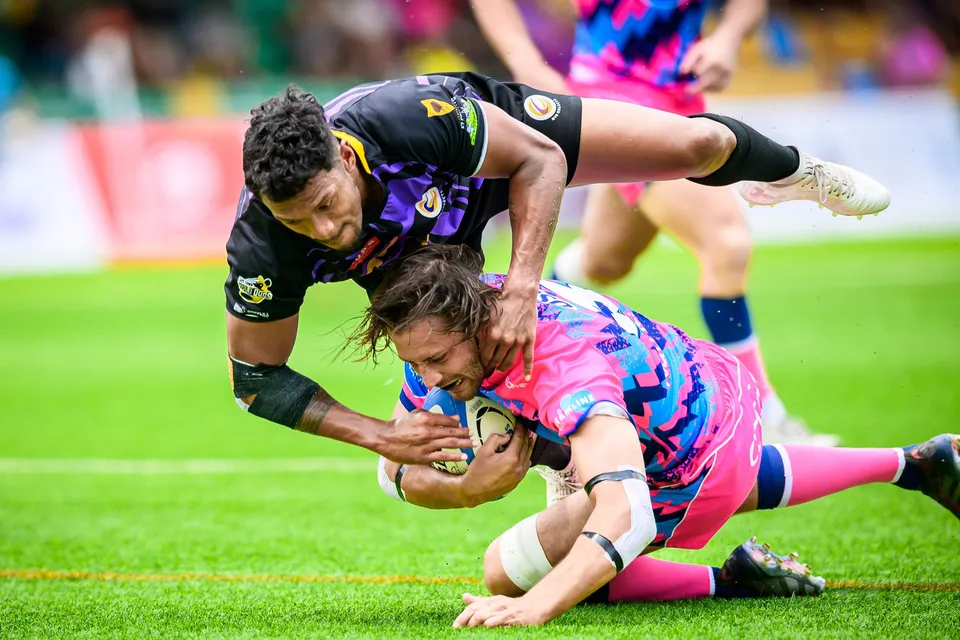 OSOB player lands on the grass clutching the ball as a purple-kit defender falls across him near the line