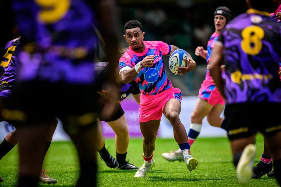 OSOB runner carries the ball between blurred purple-kit defenders in the foreground, with a team-mate in support