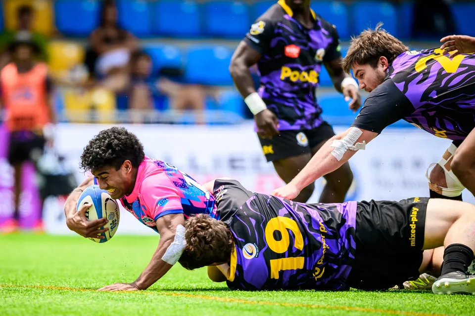 OSOB player stretches along the turf to place the ball down with a purple number 9 defender across his back