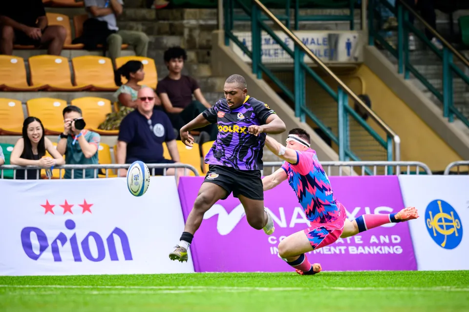 Ball bounces loose as a purple-kit runner chases it while an OSOB player slides to the grass by the Orion banner