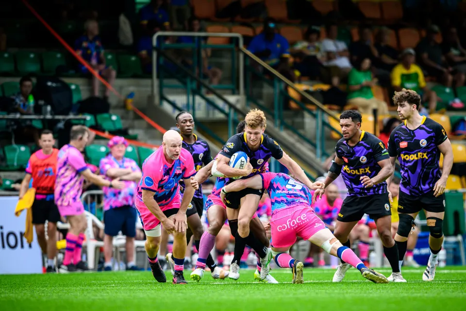 Wide view of OSOB defenders bringing down a purple-kit Rugby Tens Selects ball carrier near the touchline stand