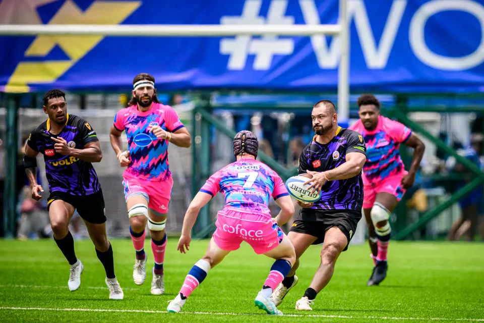 Purple-kit player is about to pass the ball as an OSOB number 7 closes in, with a team-mate running beside him