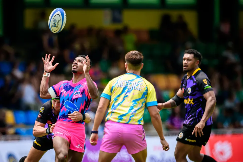 OSOB player leaps with both hands up to catch a high ball as an official in yellow and blue passes in front