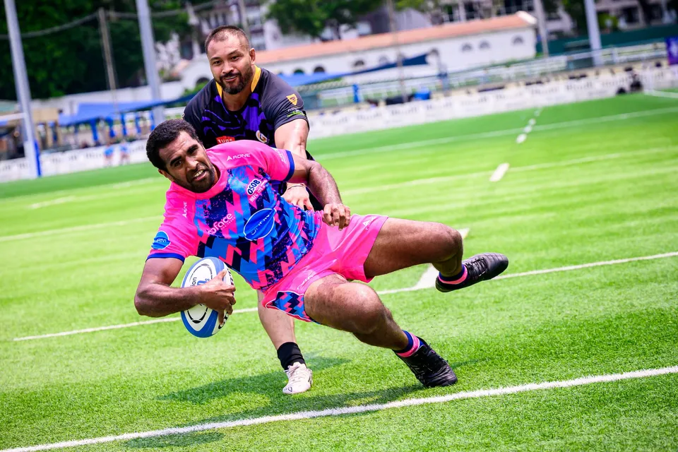 OSOB player slides along the grass to place the ball down near the touchline, a purple-kit defender trailing behind