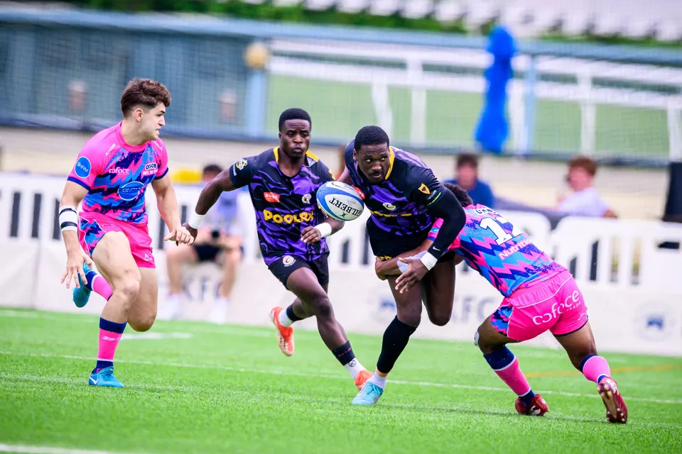Purple-kit ball carrier hands off an OSOB defender while a pink-shirted team-mate runs up on the left