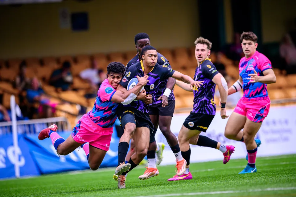Purple-kit ball carrier drives into a low OSOB tackle as more players in pink and purple converge