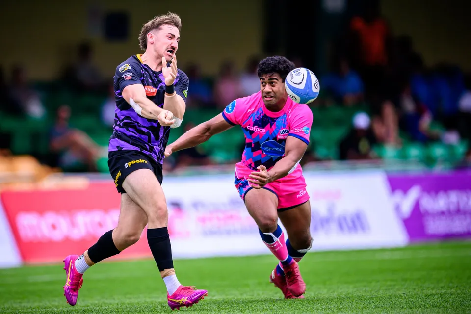 Ball flies towards an OSOB player in pink as a purple-kit opponent in the foreground grimaces