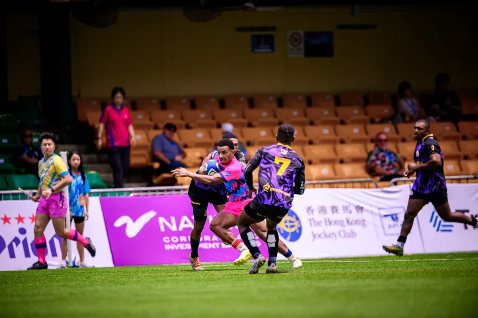 Wide shot of an OSOB player in contact with a purple number 7 in midfield, with other players running past