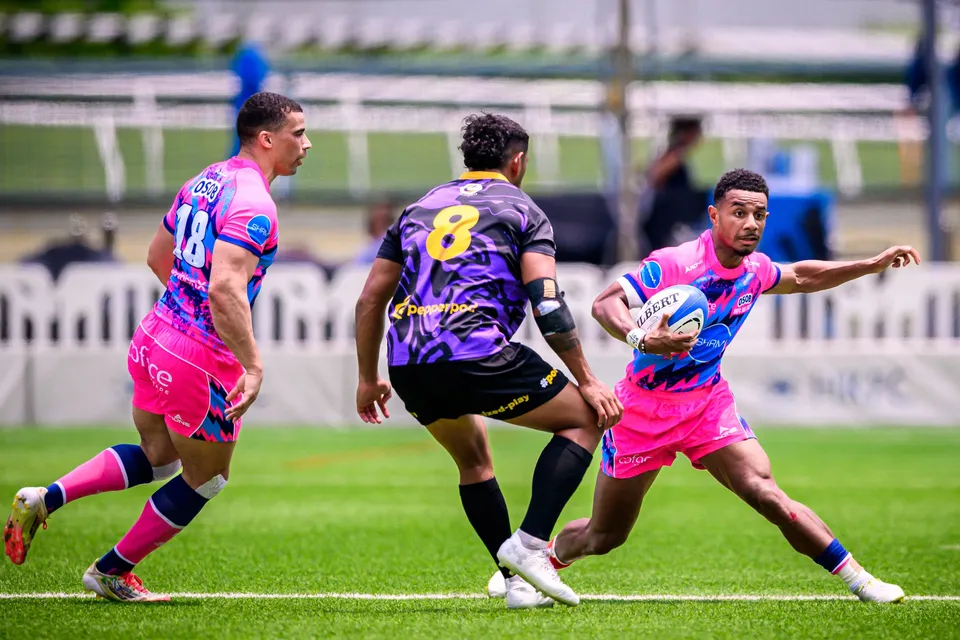 OSOB ball carrier sidesteps with the ball tucked in as a purple number 8 closes in, a team-mate running left