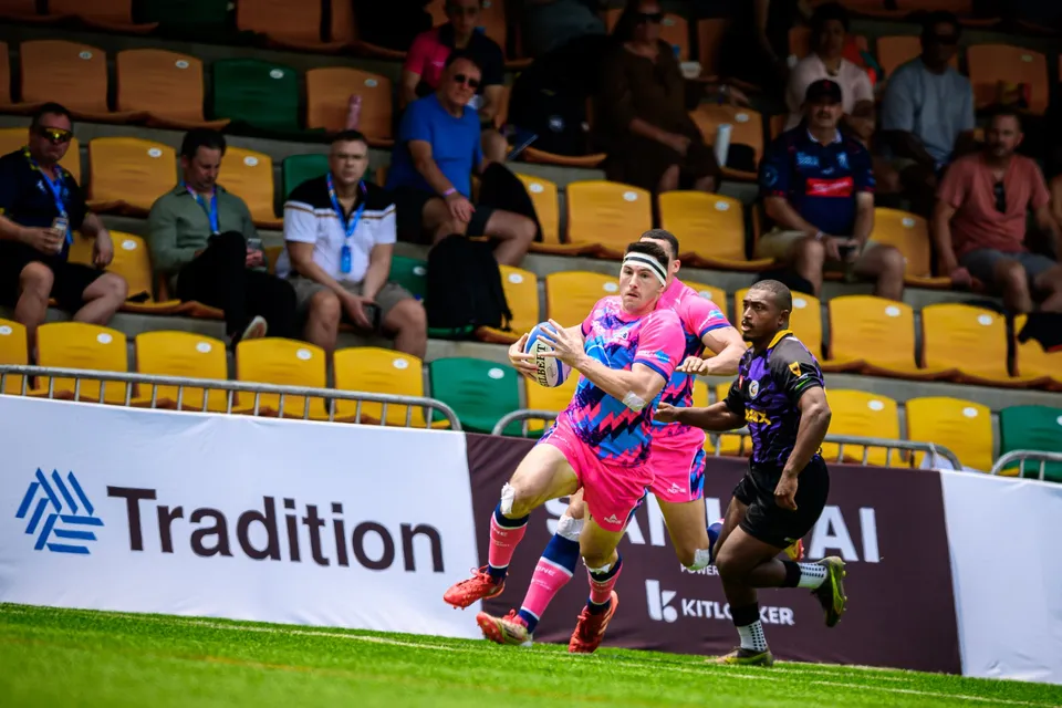 OSOB player runs the touchline with the ball, chased by a Tens Selects defender in purple, spectators in the stand