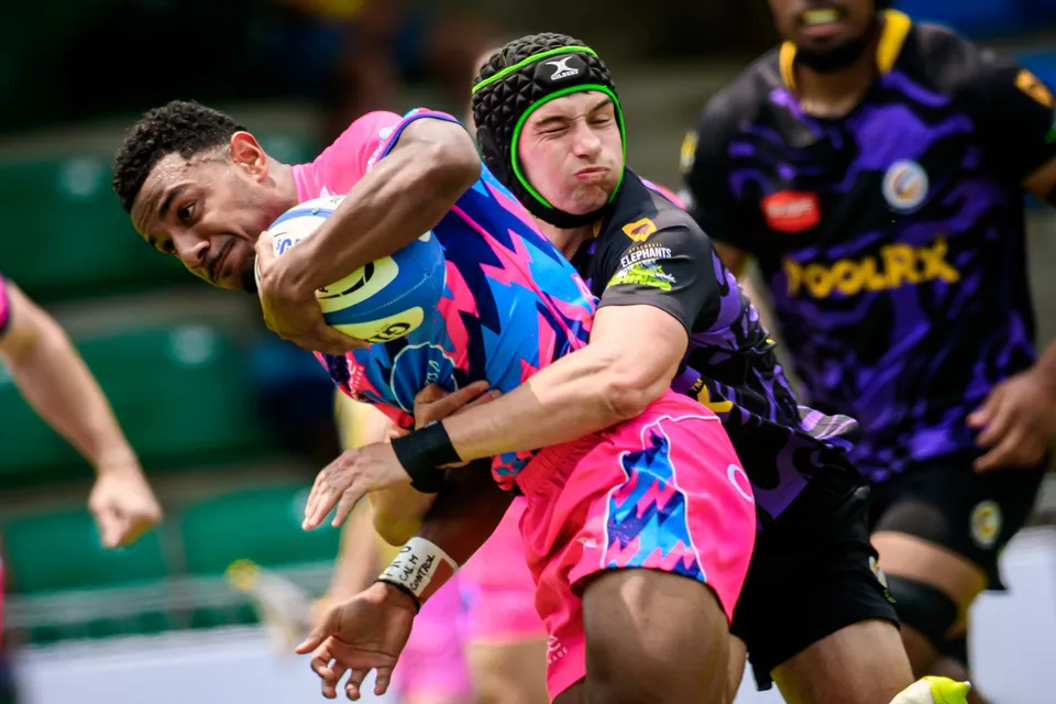 Close-up of an OSOB player gripping the ball as a Tens Selects defender in a green headguard wraps him up