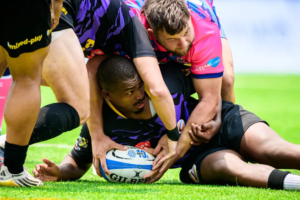 Tens Selects player lies on the grass holding the ball while an OSOB player and others pile over him