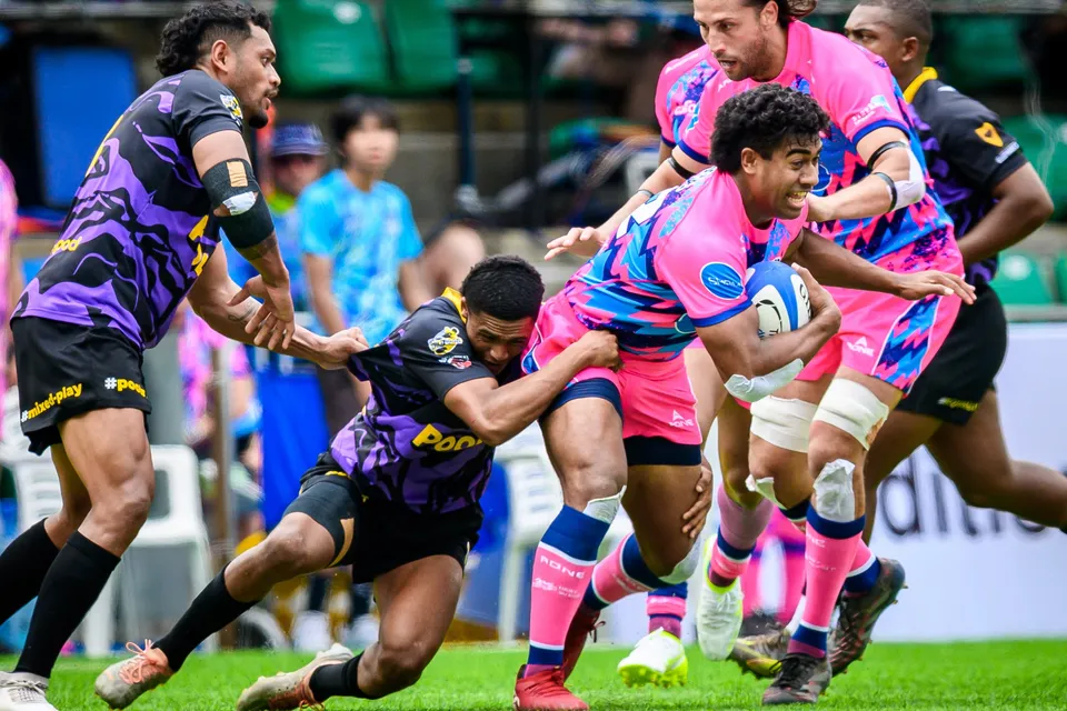OSOB ball carrier is gripped by two purple Tens Selects defenders as a pink-shirted teammate runs up in support