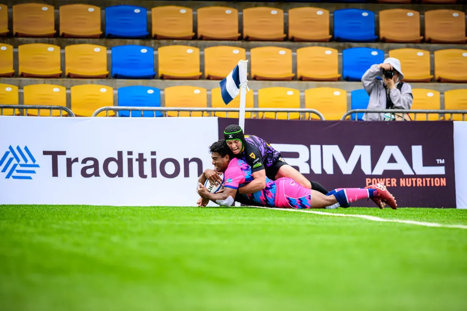 OSOB player slides towards the corner flag with the ball, tackled by a Tens Selects player in a green headguard
