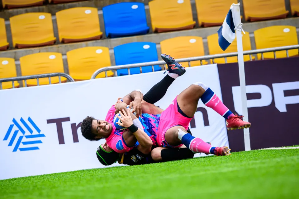 OSOB player lies by the corner flag with the ball in his arms, a defender's boot in the air above