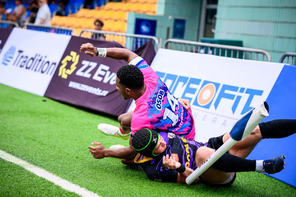 OSOB player stretches out at the touchline as a Tens Selects defender in a green headguard tackles him