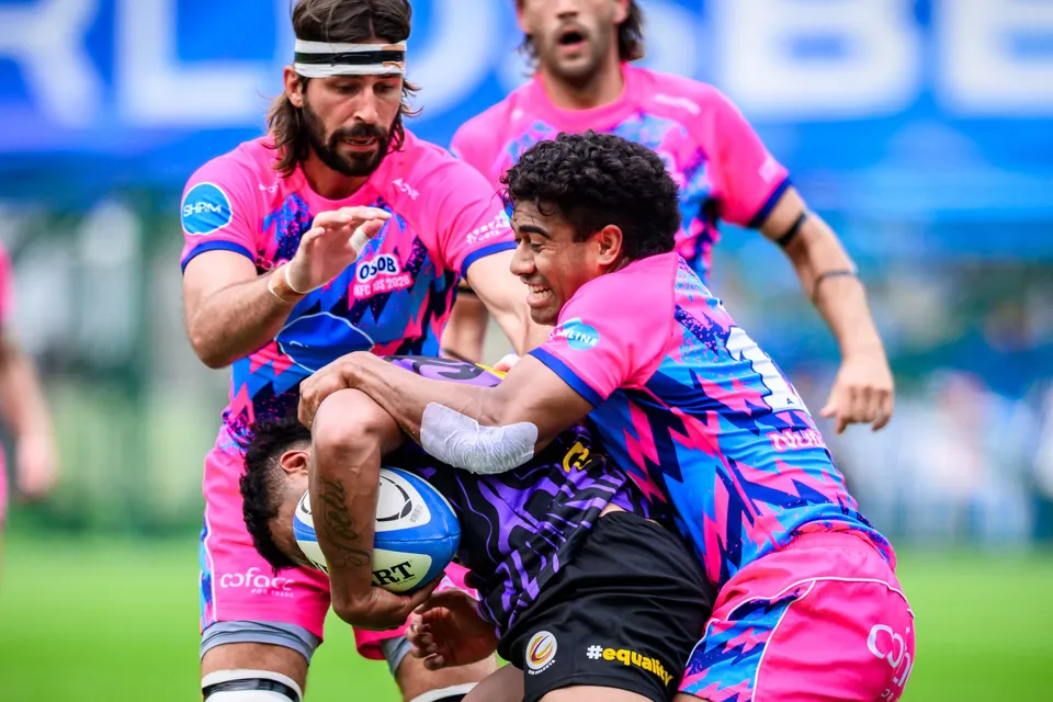 Close-up of a bearded OSOB player in a headband and a teammate tackling a Tens Selects ball carrier in purple