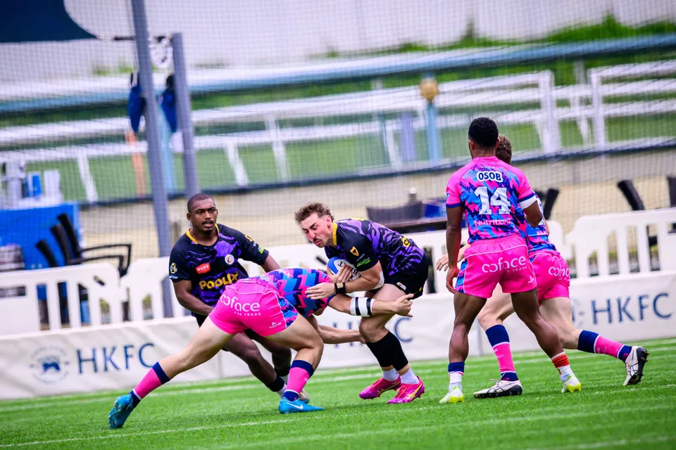 Tens Selects player in purple is tackled by OSOB players in front of HKFC boards, an OSOB number 14 close by