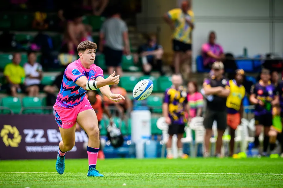 OSOB player in pink strikes a pass in mid-stride against Tens Selects, spectators and ZZ Events boards behind