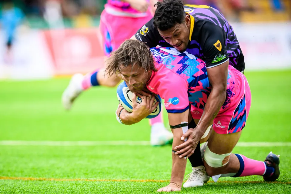 Long-haired OSOB player dives forward with the ball while a Tens Selects defender in purple hangs onto his back