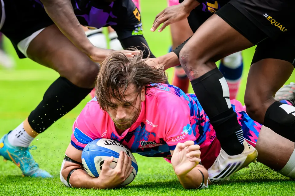 Long-haired OSOB player presses the ball down on the grass as legs of other players surround him