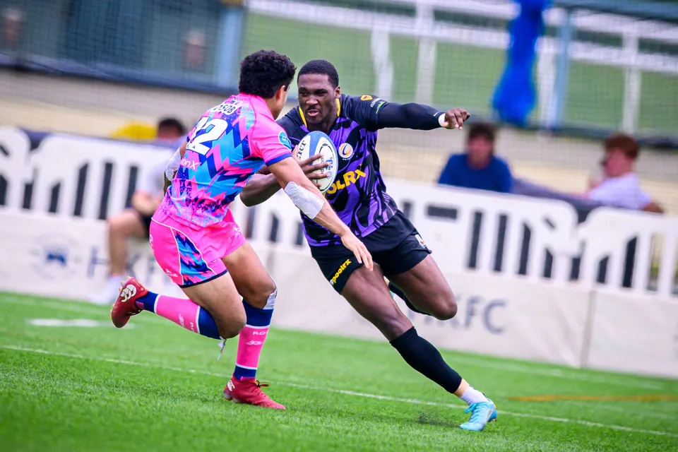 Tens Selects player in purple runs with the ball at an OSOB number 12 in pink beside the HKFC boards