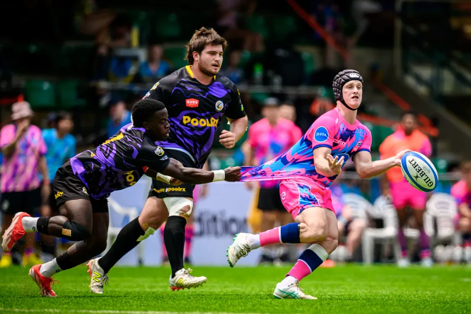 OSOB player in a headguard passes the ball as a Tens Selects player on the ground grabs hold of his shirt