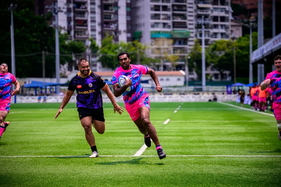 OSOB player sprints with the ball down the pitch, a Tens Selects defender trailing, apartment blocks behind