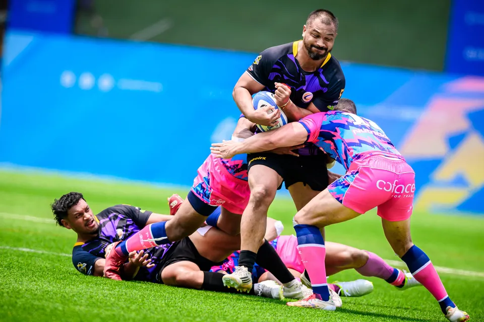 Bearded Tens Selects ball carrier is tackled by two OSOB players while a player lies on the grass at his feet