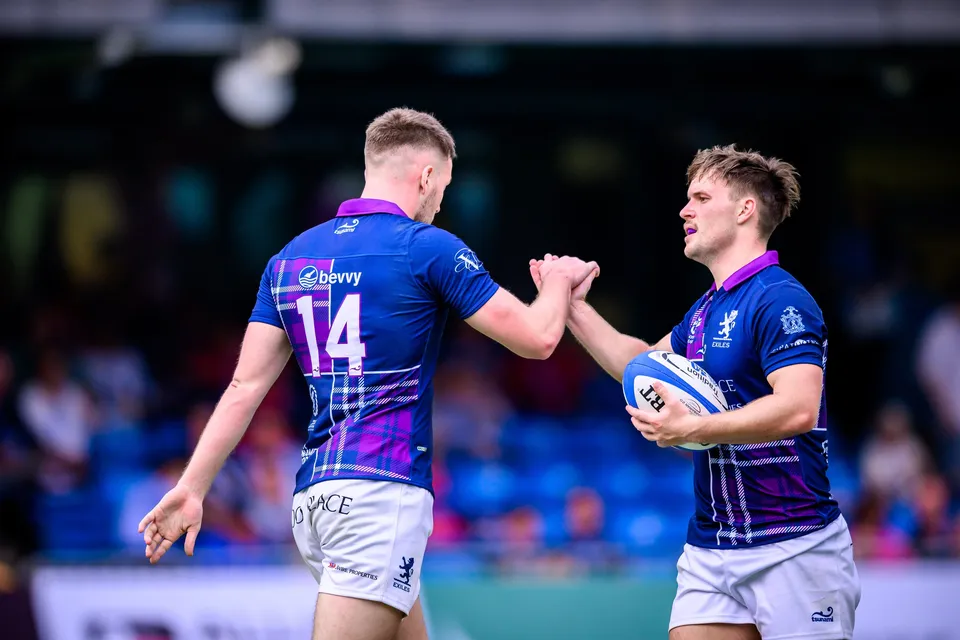Scottish Exiles number 14 and a teammate holding the ball share a high five in front of blue stadium seats