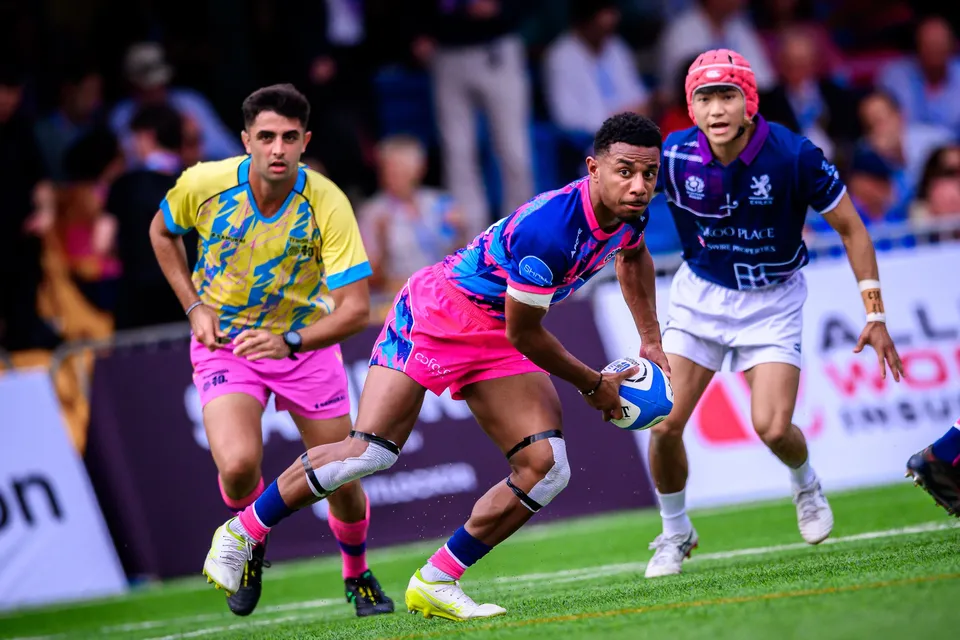 OSOB ball carrier in pink holds the ball one-handed as a teammate in yellow and blue supports, Exiles player right