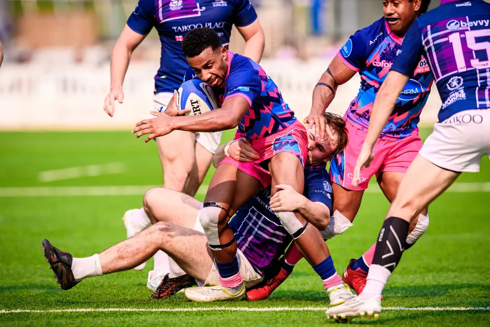 OSOB ball carrier is hauled down in a pile of players on the grass as Exiles number 15 closes in