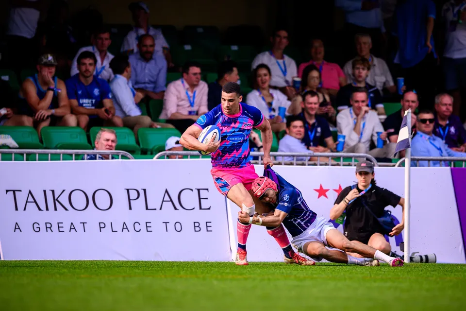 OSOB runner in pink is brought down by a sliding Exiles defender in a red cap by a Taikoo Place board