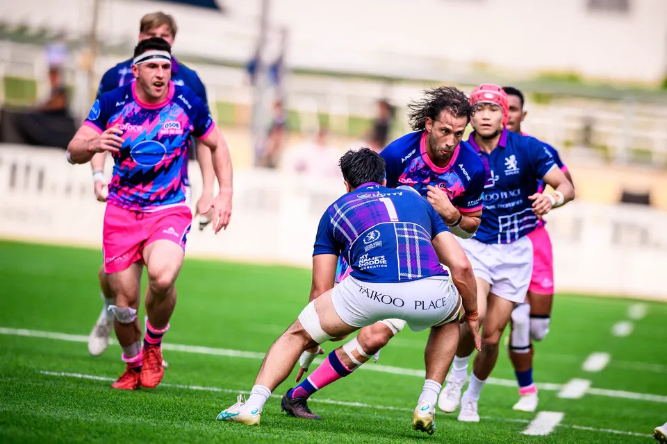 OSOB ball carrier with the ball tucked under his arm is tackled at the waist by an Exiles player, more Exiles behind