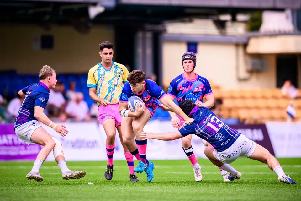 OSOB ball carrier is tackled low by Exiles number 13 as a headguard teammate and a yellow-blue player watch