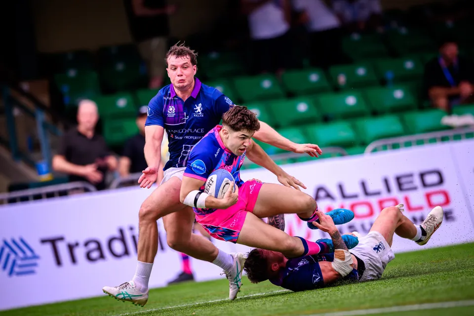 OSOB ball carrier in pink and blue dives low over a fallen defender against Taikoo Place Scottish Exiles, 2026