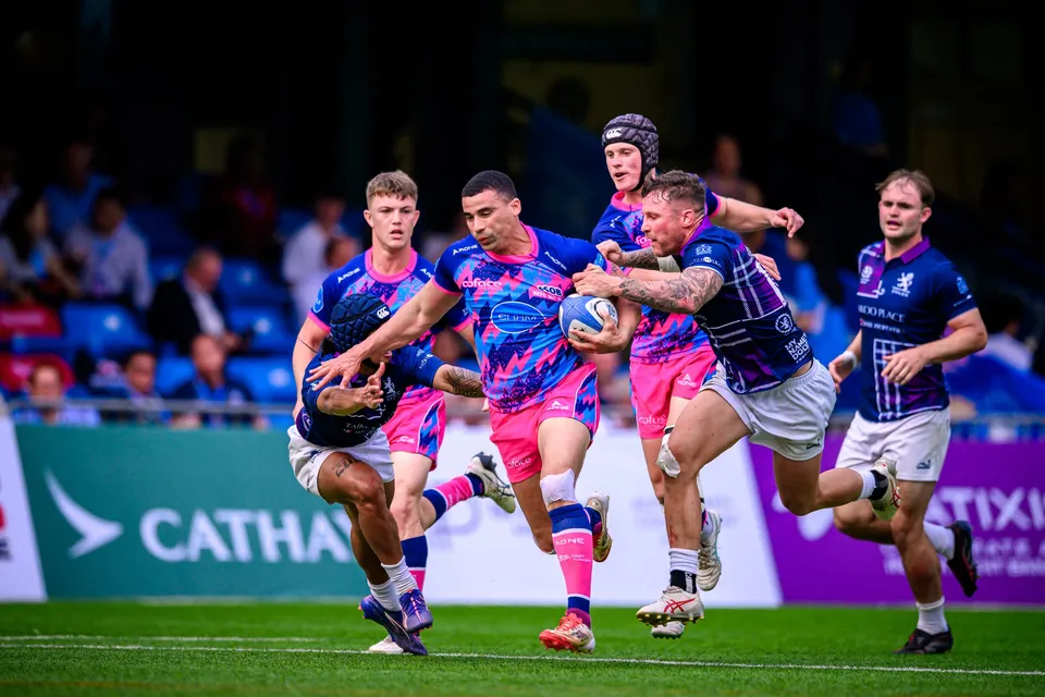 OSOB runner in pink and blue pattern carries the ball at Scottish Exiles defenders in front of a Cathay banner