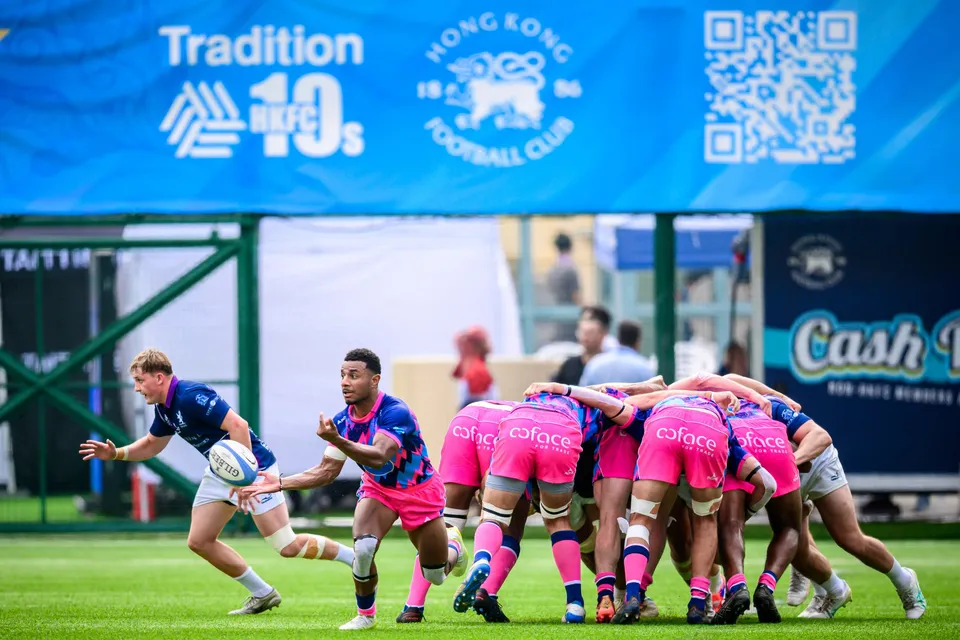 OSOB scrum-half in pink passes from the base of a pink-shirted ruck below a Tradition HKFC 10s banner