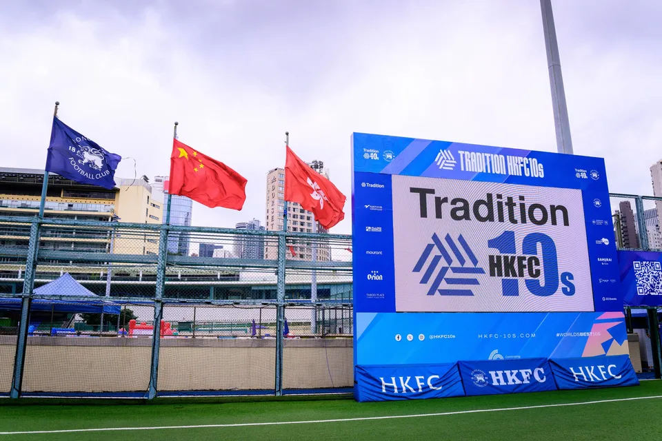 Large Tradition HKFC 10s scoreboard screen beside three flags and a city skyline at the pitch edge