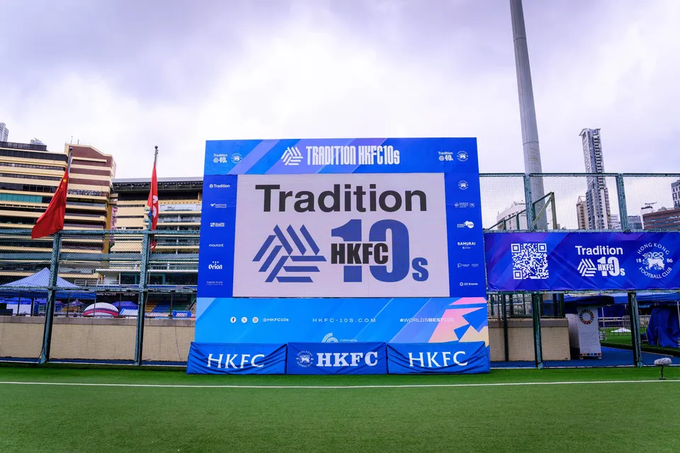 Tradition HKFC 10s event screen and a QR code banner at the end of the pitch under a cloudy sky