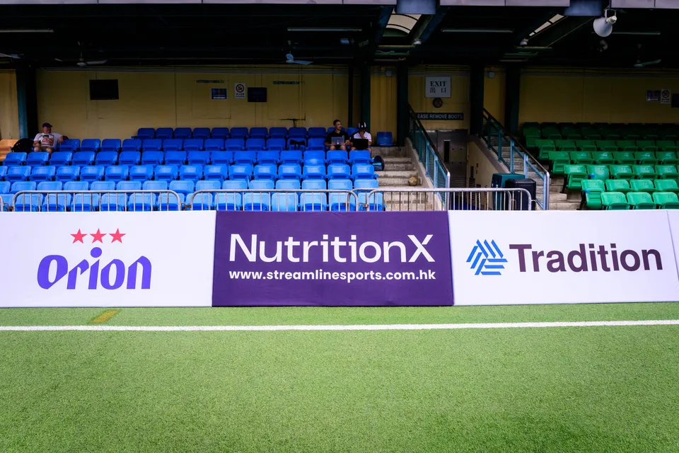 Orion, NutritionX and Tradition boards along an empty stand, with two spectators in the blue seats