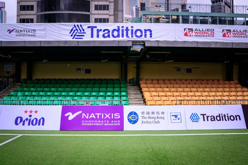 Wide view of a covered stand with Natixis and Tradition banners above Orion, Natixis and Jockey Club boards