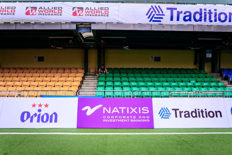 Allied World Insurance, Orion and Natixis boards in front of orange and green stand seats and a lone spectator