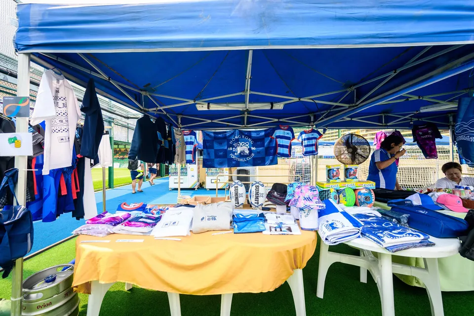 Fan Zone sign in English and Chinese pointing to games and food, with blue marquees and a barrier behind