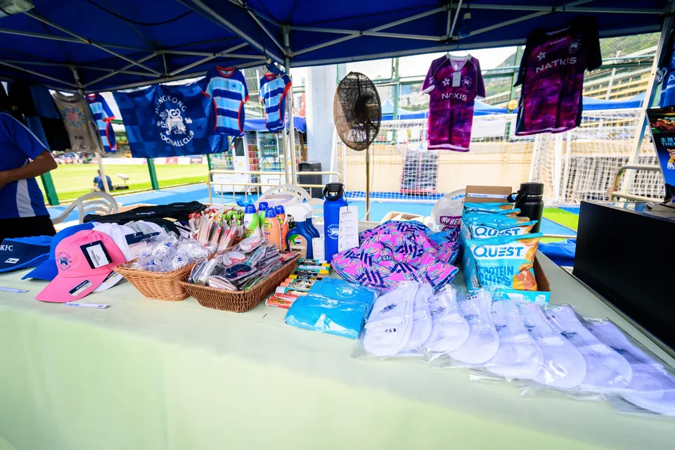 Stall counter with shirts hanging behind, a basket of snacks, pink caps and folded white towels