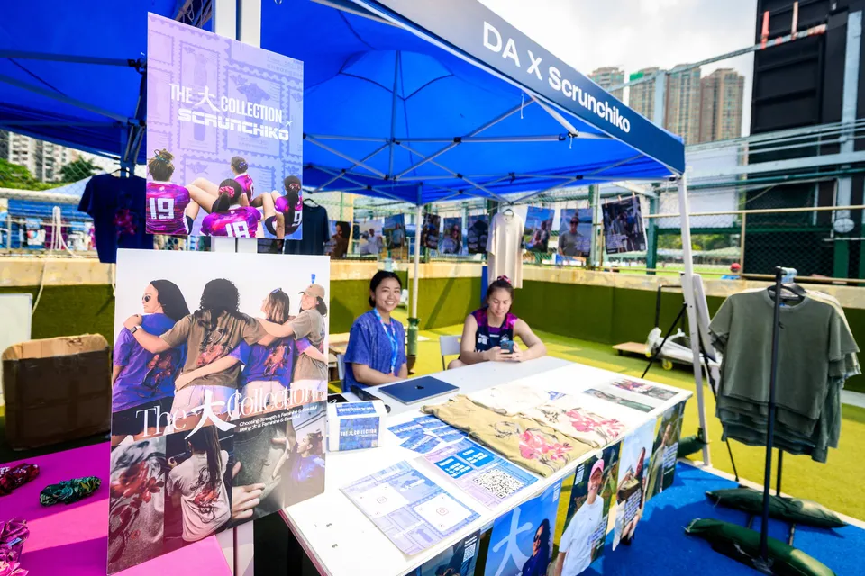 Scrunchie stall with a poster of women in pink and blue kit, and a woman seated at a table behind it